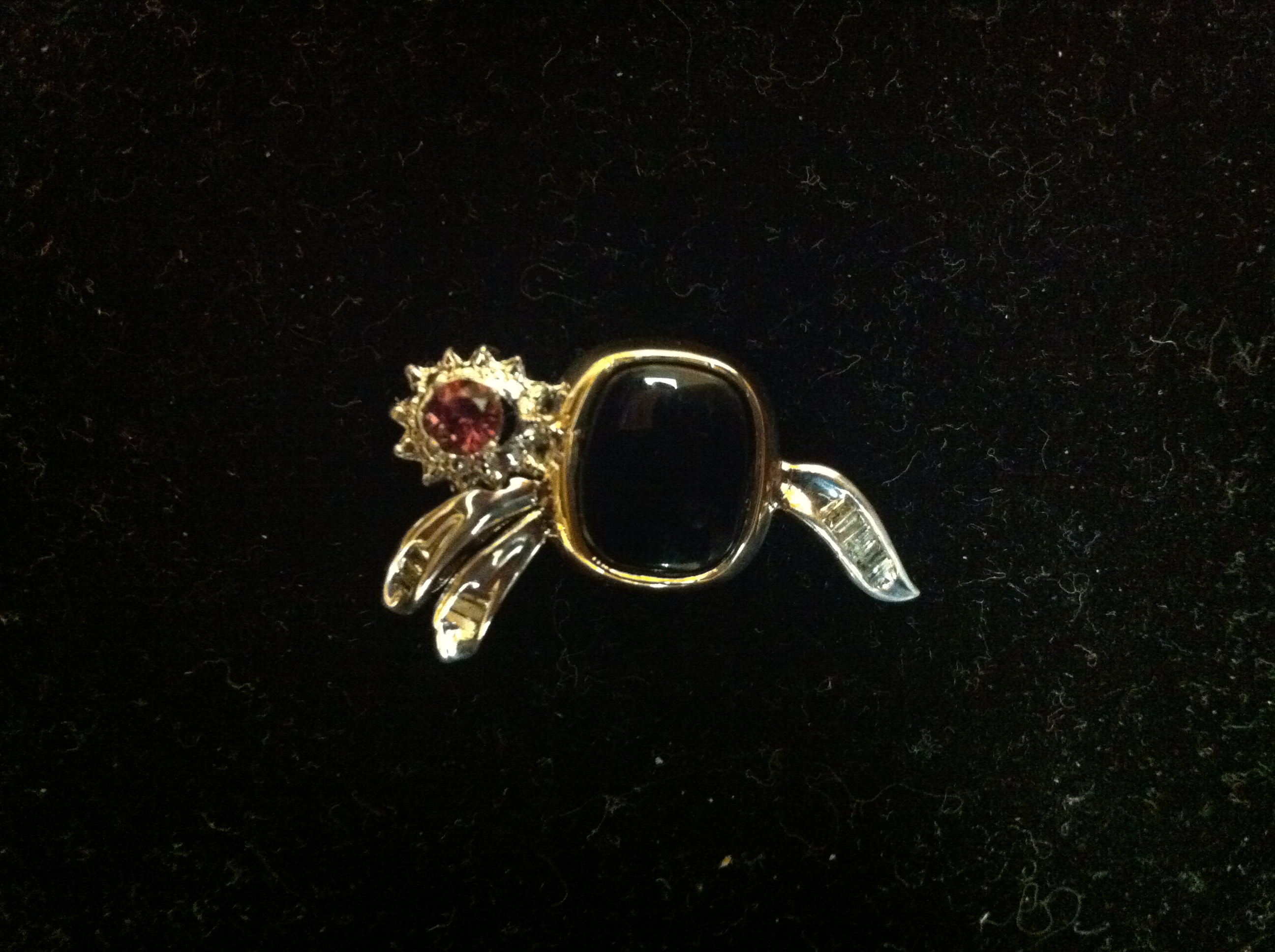 A gold pin with a black stone and a red stone