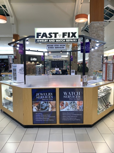 Fast-Fix kiosk in Manassas mall. Hexagonal shape with glass cabinets on the sides and wood center with Jewelry and Watch repair services signs