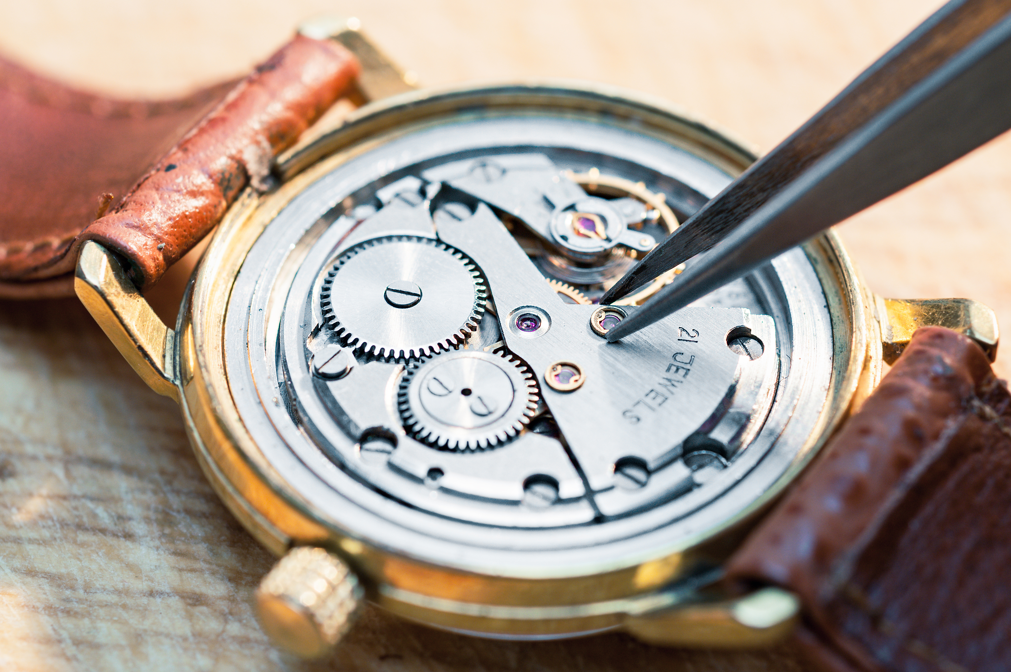 A gold watch with brown leather band appears open and you can see the mechanics of it.